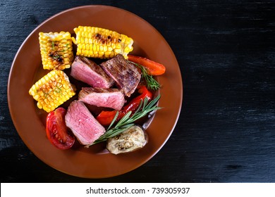 Slices of mildly fried steak with corn and vegetables. Black background. Top viewThe concept of natural traditional food.