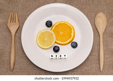 Slices Of Orange And Lemon With Blueberries On A White Ceramic Plate With Wooden Folk And Spoon. White Cube Letters Spelling A Word DIET. Flat Lay Photography On Dietary Concept.