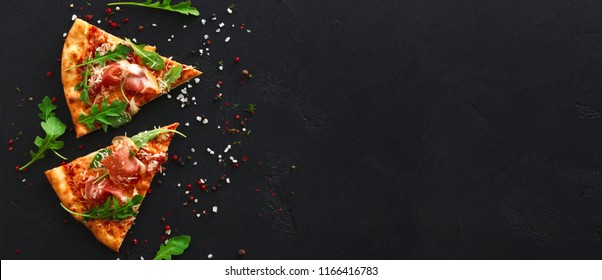 Slices of pizza with prosciutto and spices on black background, copy space, top view