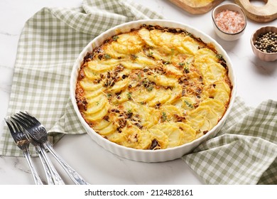 Slices potato casserole with red onions, fresh thyme and rosemary on green checkered kitchen towel , wooden board with flavoring ingredients: pepper, salt, olive oil