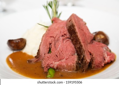 Slices Of Rare Prime Rib On A White Plate With Mushroom Gravy, Asparagus And A Rosemary Garnish