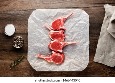 Slices Of Raw Lamb Rib Chops On White Cooking Paper And Wooden Table. Decorated With Salt, Pepper, Meat Fork And Napkin. Overhead View.