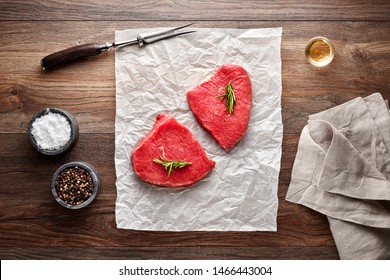 Slices Of Raw Roast Beef On White Cooking Paper And Wooden Table. Decorated With Salt, Pepper, Meat Fork And Napkin. Overhead View.