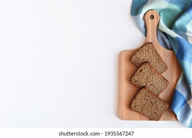 Slices of rye bread on a wooden cutting board on a blue napkin and white textured background. Top view, copy space. Flat lay. Healthy eating concept.