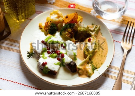 Slices of soft moist cornbread with yogurt sauce sprinkled with pomegranate seeds served with vegetable garnish of baked potatoes, cauliflower and broccoli. Albanian cuisine