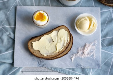 Slices of sourdough bread with butter, salt, egg and cup of coffee on grey board, selective focus, copy space. Beautiful simple breakfast. Top view.
