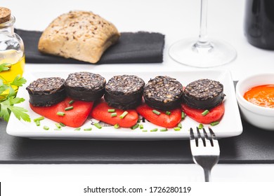 Slices of Spanish black pudding on piquillo peppers in white plate on white background. Spanish tapas.
