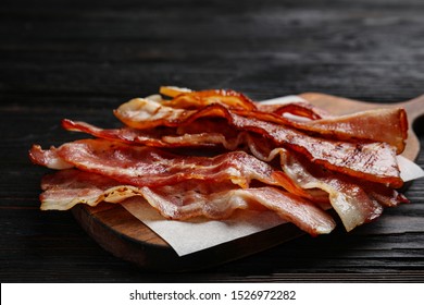 Slices of tasty fried bacon on black wooden table, closeup