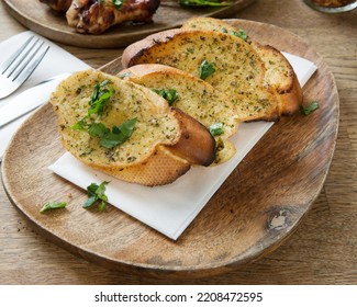 Slices Of Toasted Bread With Garlic And Herbs On Wooden Plate In A Restaurant Table. Side View.