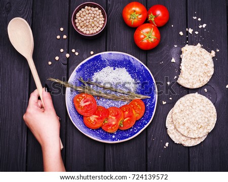 Slices of tomatoes in blue plate and spices. A wooden spoon in a woman's hand. Fragrant pepper in a wooden toe on a dark background. Close-up. Food concept.