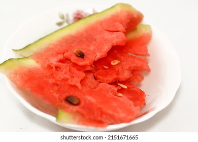 Slices of watermelon fruit cuts into pieces with seeds and its green shell served in a white plate as a healthy fresh snack, selective focus of a stack of  fresh ripe watermelon isolated on white