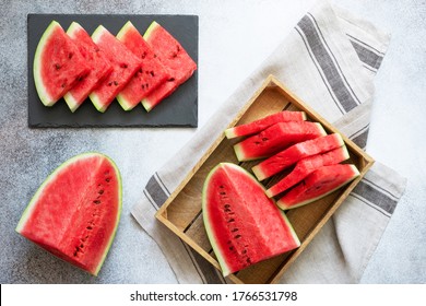 Slices of watermelon on the black plate and pieces of watermelon on the wooden tray on the concrete background. Flat lay.