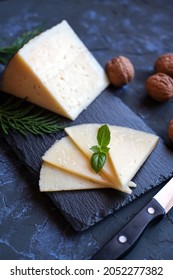 Slices And Wedge Of Cured Cheese With Walnuts On Dark Background From Above