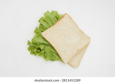 Slices of white bread placed beside a pile of green lettuce leaves on a clean white background, representing sandwich ingredients and simple meal preparation.
