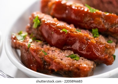 Slicing classic meatloaf with a sweet glaze on a white serving plate - Shutterstock ID 2205896683