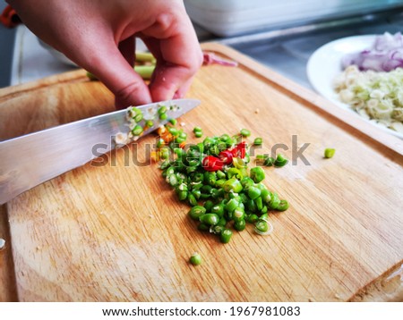 Slicing green and red chilli on wooden plate. Spicy food.