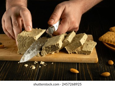 Slicing halva for dessert with a knife in the hands of a chef. A cook cuts halva on a kitchen board before preparing a sweet breakfast.