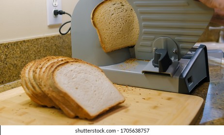 Slicing Homemade Bread With An Electric Deli Slicer Machine. Cutting Organic Bread Loaf Into Sandwich Slices Using Home Kitchen Appliance.