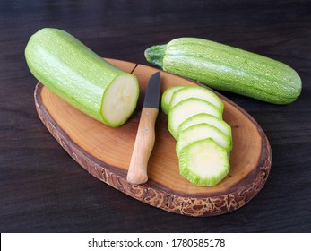Slicing zucchini on wooden board over dark table