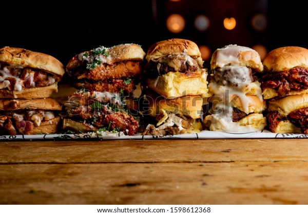 Sliders. Traditional classical American diner\
or bar food menu item, favorite a variety of beef hamburger\
sliders. Variety of beef sliders lined up, in a restaurant bar, w/\
lights in the\
background.