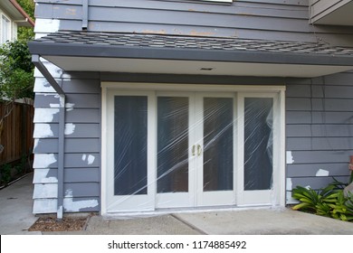 Sliding Glass Door Covered In Plastic Repairs To Cracked Peeling Wood Siding With Primer Preparing For Painting. Properly Painting Can Help Protect Against Moisture And Insect Damage.