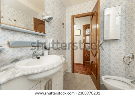 A slightly dated full bathroom with a square mirror, vintage tiles with blue accents and a gray marble countertop