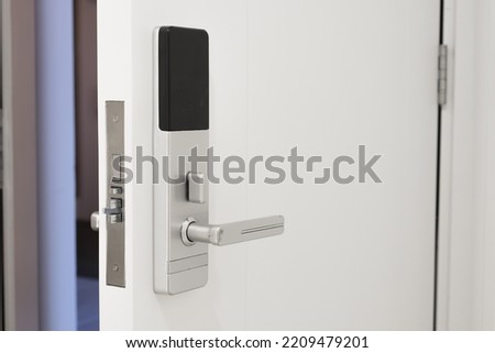 Slightly open white door to the hotel room with a Electronic magnetic lock. Electronic hotel lock with wireless reader. Chrome-plated handle on the interior door.