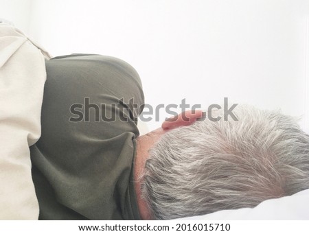Slightly overexposed photo showing back head part of an elderly man wearing t-shirt sleeping in bed with pillow and duvet with copy space for runaround or wraparound text 