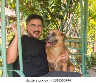 A Slightly Overweight Man In A Black Shirt And His Pet Dog Sitting At An Outdoor Swing By The Patio.