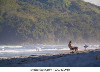 Slightly Overweight Man Sitting On A Beach Chair Looking At The Waves