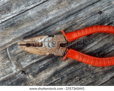 A slightly rusty pliers with a red handle on a shabby bamboo wood