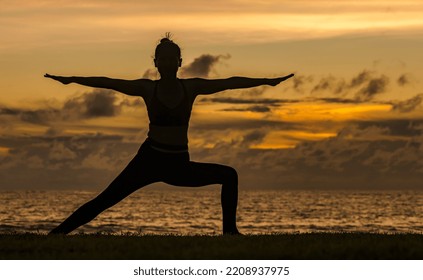 Slihouette yoga woman doing exercise at Phuket beach watching sunset,sporty female working out with yoga pose in front of sea, woman exercising warrior pose, female outdoor fitness on beach concept