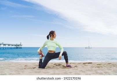 Slim 40 years old black haired female in activewear doing twisting with support leg while practicing yoga on sandy beach near pier - Powered by Shutterstock