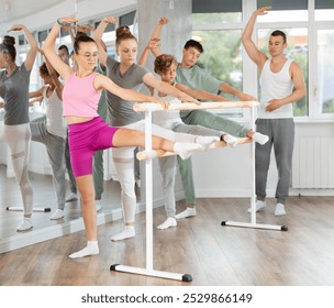 Slim adolescent attendees of ballet courses doing leg stretching exercise under control of ballet-master in dancehall - Powered by Shutterstock