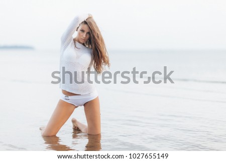 Slim appealing gorgeous woman wears white summer clothing, poses against beautiful sea view, keeps hand on head, breathes fresh air, copy space for your advertising content or promotional text