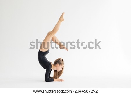 slim artistic teenager girl in black leotard trains on white background in rhythmic gymnastic exercise, children's professional sports