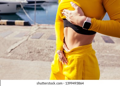 Slim athletic girl in a stylish yellow tracksuit and smartwatch shows her flat beautiful belly after a street workout on a sunny warm summer day. Sport and motivation concept