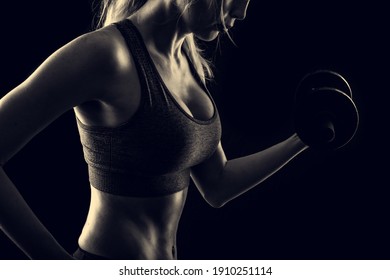 Slim athletic woman on black background in gym. Holding dumbbell in the hand