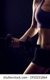 Slim athletic woman on black background in gym. Holding dumbbell in the hand