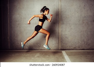 Slim attractive sportswoman running  against a concrete wall - Powered by Shutterstock