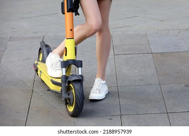 Slim Bare Legs Of Girl Standing With Electric Scooter On A Street. Riding E-scooter In Summer City