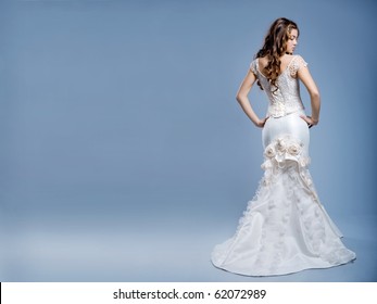 Slim beautiful woman with long hair wearing luxurious wedding dress over gray studio background