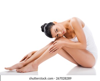 Slim beauty. Beautiful young woman looking at camera and holding hands on her legs while sitting against white background  