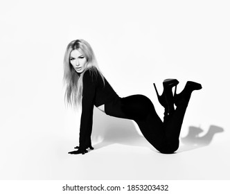 Slim Blonde Woman With Pouty Lips In Tight Black Overall Suit And High-heeled Shoes Stands On All Fours And With Feet Up Sexy Posing. Black And White Full-growth Portrait