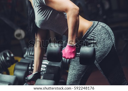 Slim, bodybuilder girl, lifts heavy dumbbell standing in front of the mirror while training in the gym. Sports concept, fat burning and a healthy lifestyle.