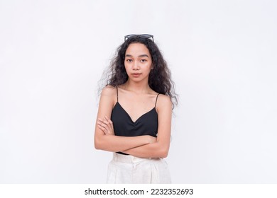 A slim and confident Filipino woman with long curly hair in her early 20s. Wearing a black spaghetti strap blouse and white pants. Arms crossed. Isolated on a white background. - Shutterstock ID 2232352693