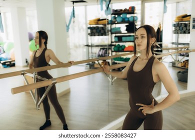 Slim female in activewear performing exercise on barre while stretching legs against mirror during gymnastic class in studio