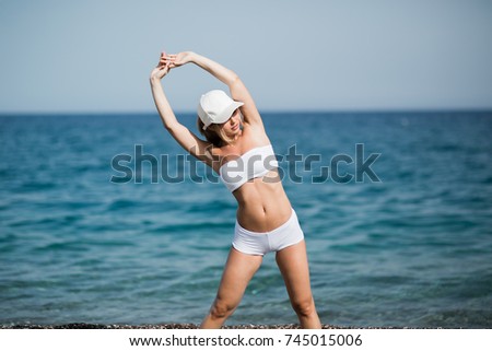 Slim female girl with beautiful figure is doing stretching exercise on the beach, morning run, fitness and healthy lifestyle concept