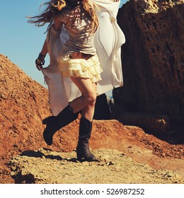 Slim female legs dressed in leather cowboy shoes with short lace skirt, fashion woman dancing on a rocks 