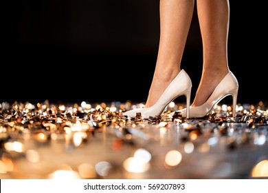Slim female legs in high-heeled shoes standing on golden confetti